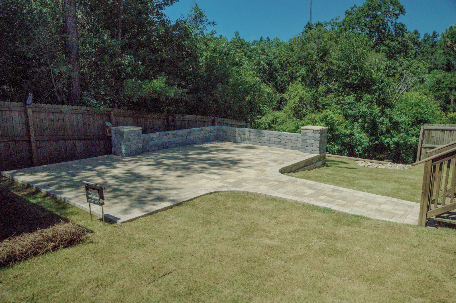 Wide view of a finished paver patio and block retaining wall across a backyard in Baldwin County, Alabama