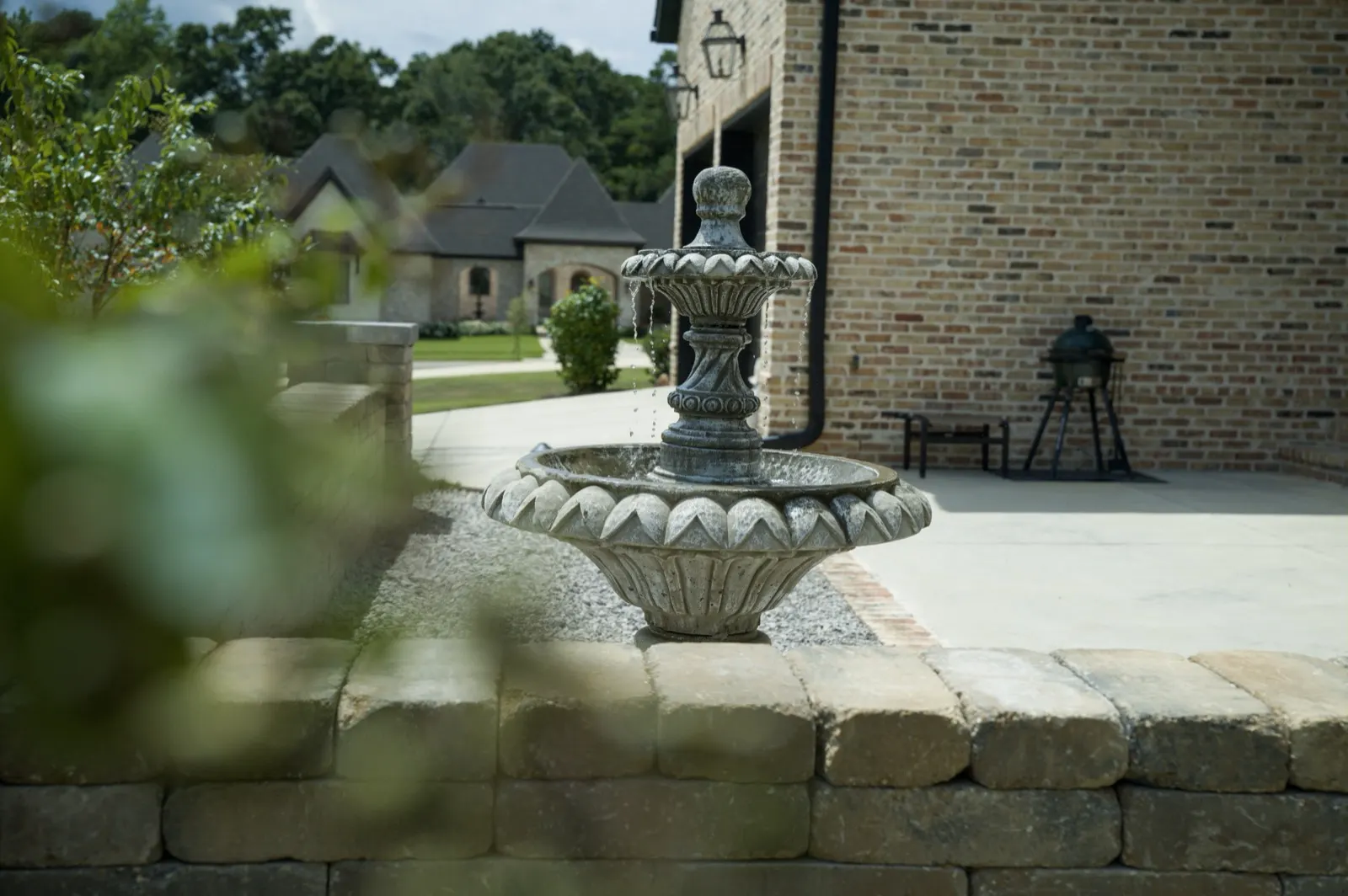 Tiered stone fountain on white gravel beside a brick home in Fairhope, Alabama, seen over the stone seat wall