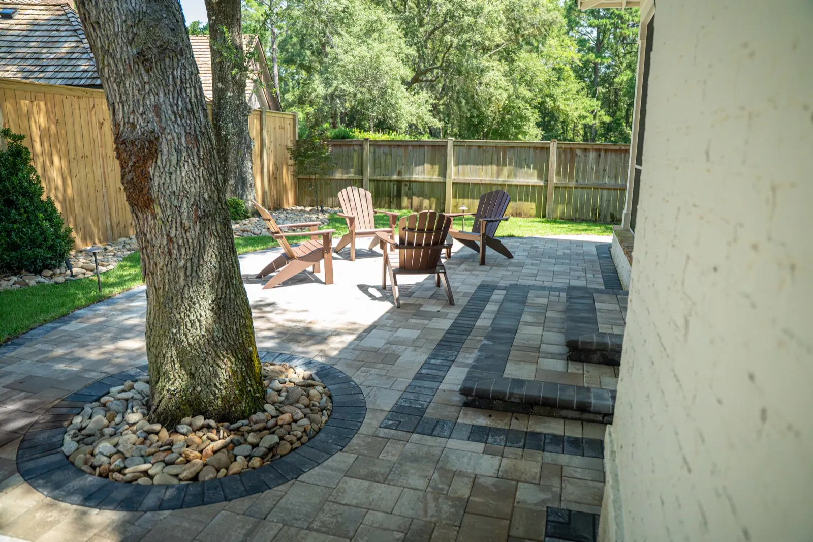 Dark paver border ringing a river rock bed cut around a tree in a Point Clear, Alabama patio