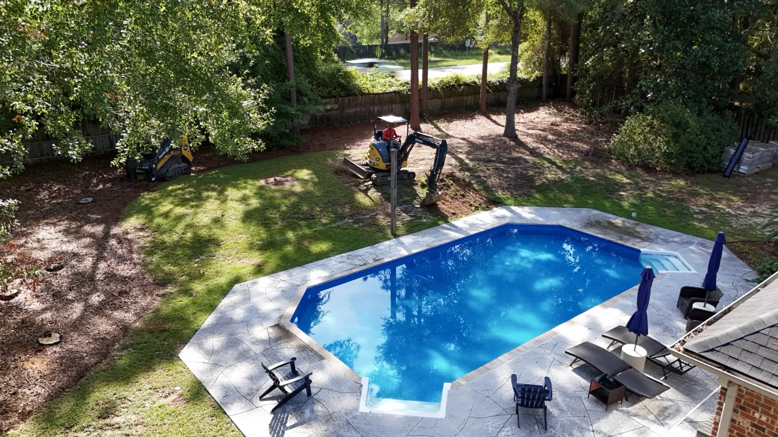 Mini excavator digging drainage work in a backyard near a pool in Baldwin County, Alabama