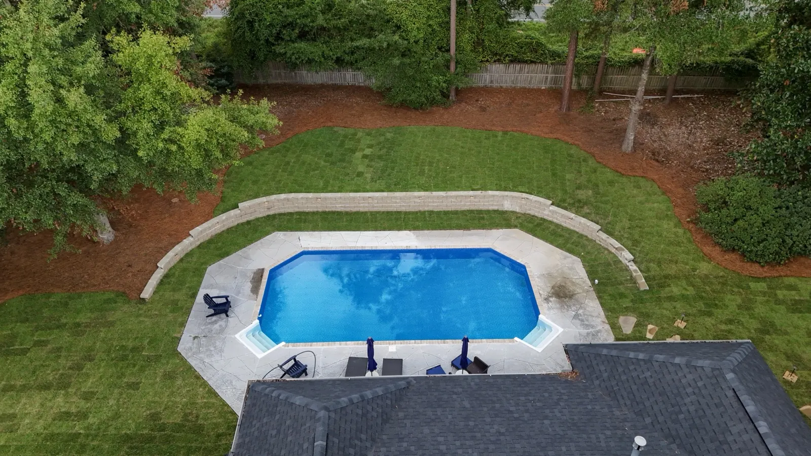 Aerial view of a concrete pool deck wrapped by a curved retaining wall at a Baldwin County, Alabama backyard